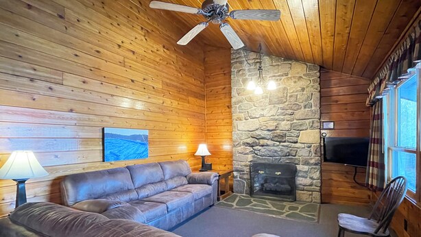 A cozy cabin interior with a stone fireplace, leather sofa, and a television. - Charming Lake View Cabin in the Poconos on Private Resort (Stroudsburg)