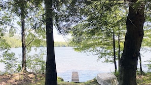 A secluded lakeside campsite with a clear view of the water, surrounded by tall trees and a covered tent. - Charming Lake View Cabin in the Poconos on Private Resort (Stroudsburg)