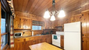 A wooden cabin kitchen with a wooden table, white appliances, and a hanging light fixture. - Charming Lake View Cabin in the Poconos on Private Resort (Stroudsburg)