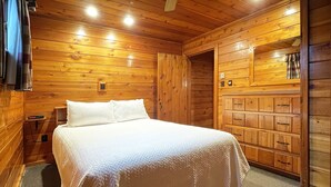 A wooden cabin room with a bed, a nightstand, a dresser, and a small shelf with a clock. - Charming Lake View Cabin in the Poconos on Private Resort (Stroudsburg)