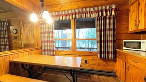 A wooden cabin interior with a wooden table, bench, and a microwave on a cabinet. - Charming Lake View Cabin in the Poconos on Private Resort (Stroudsburg)