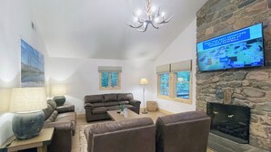 Una sala de estar con chimenea de piedra, un televisor de pantalla plana grande montado en la pared, un sofá de cuero marrón y una mesa de centro.