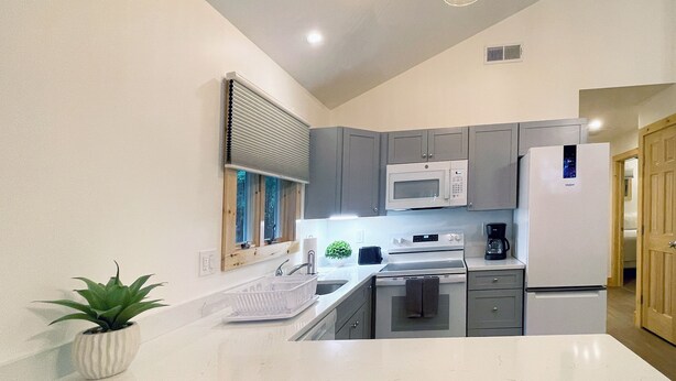 Una cocina moderna con gabinetes grises, una encimera blanca, un microondas, un refrigerador y un lavamanos.