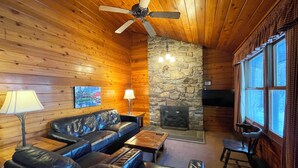 Un intérieur de chalet chaleureux avec une cheminée en pierre, un canapé en cuir et un téléviseur.