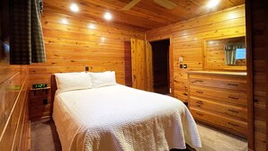 Une chambre à coucher aux murs lambrissés, comprenant un lit, une table de chevet, une commode et un miroir.