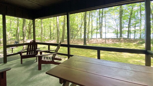 Un espace extérieur abrité, doté de bancs en bois et de tables de pique-nique, offrant une vue sur une zone boisée.