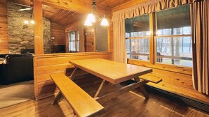 Une cabane en bois avec une grande table et des bancs, des murs en pierre et de grandes fenêtres.