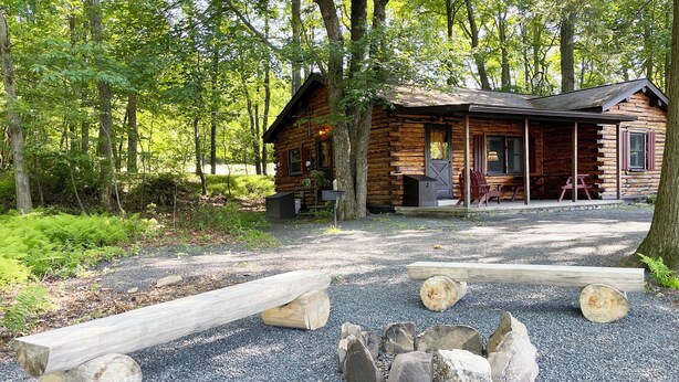 Un rustico chalet con veranda, circondato da alberi e ghiaia.