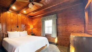 Una camera in legno con un letto, un comodino, una lampada, una finestra con tende e una ventola a soffitto.