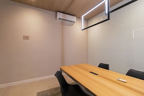 Un salón de conferencias con una mesa de madera, sillas negras y un equipo de aire acondicionado en la pared.