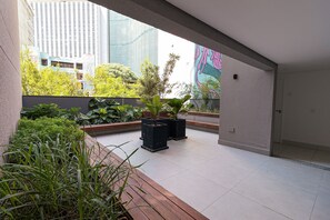 Un espacio interior moderno con vistas a edificios altos, suelo de baldosas y diversas plantas.