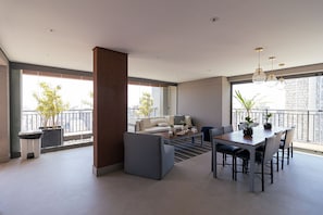 A modern living room with a dining area, large windows, and a view of the city.