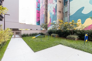 A pathway leading to a building with colorful murals, a small playground, and well-maintained greenery.