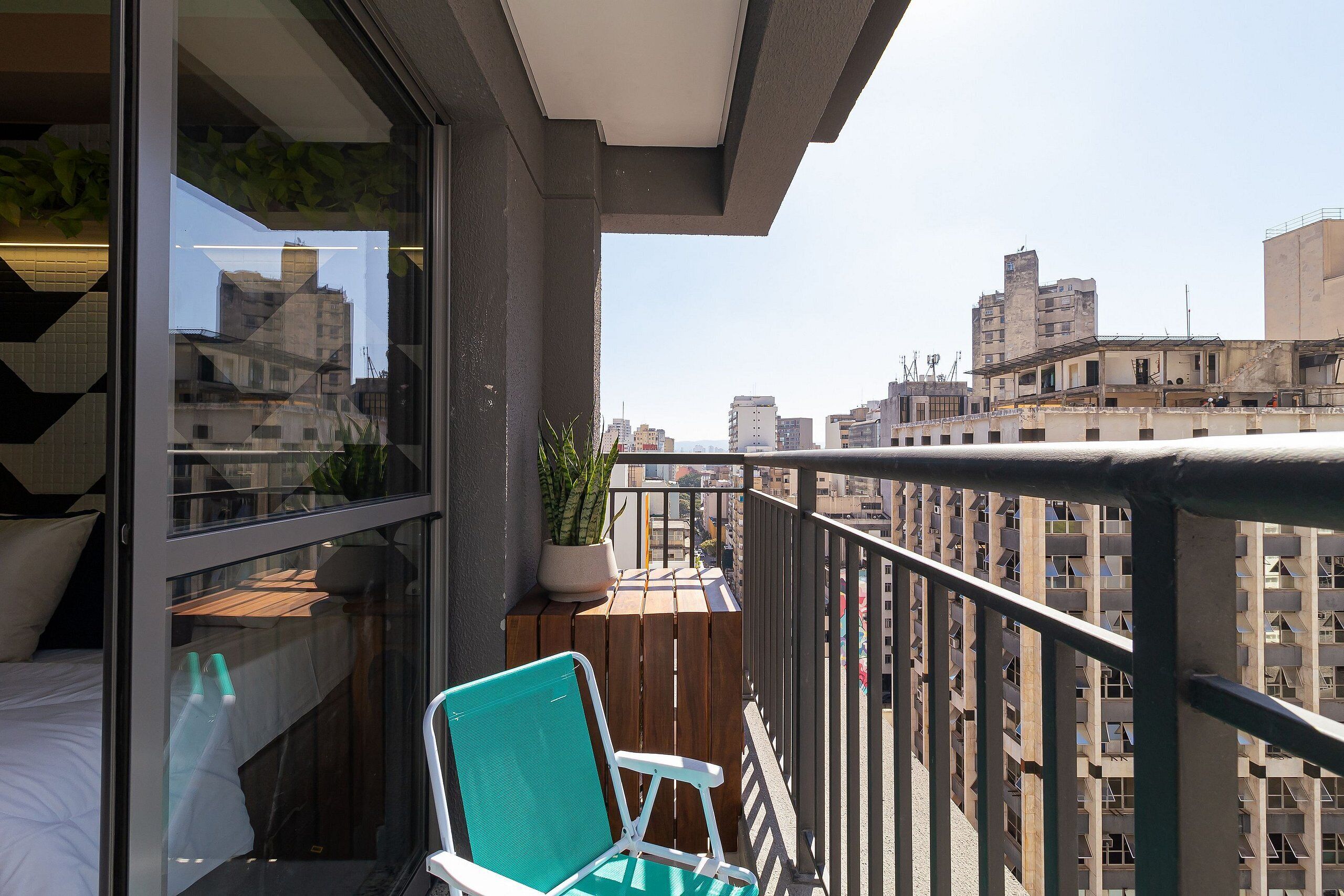 A balcony with a wooden table, a potted plant, and a green chair.