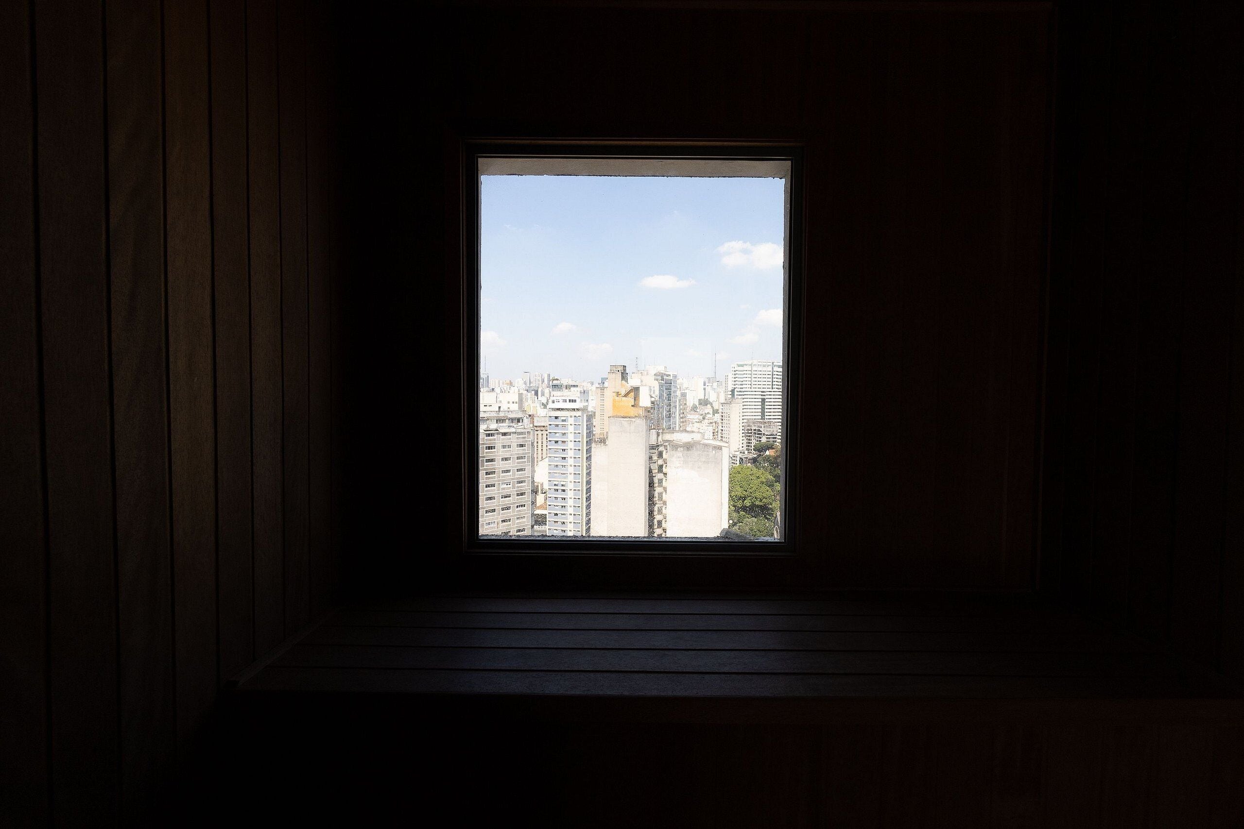 Una ventana con vistas a un paisaje urbano, paredes de madera y suelo oscuro.