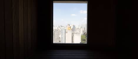 A window with a view of a cityscape, wooden walls, and a dark floor.