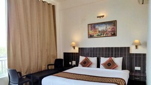 A hotel room with a bed, a desk, two chairs, a painting on the wall, and two wall lamps.