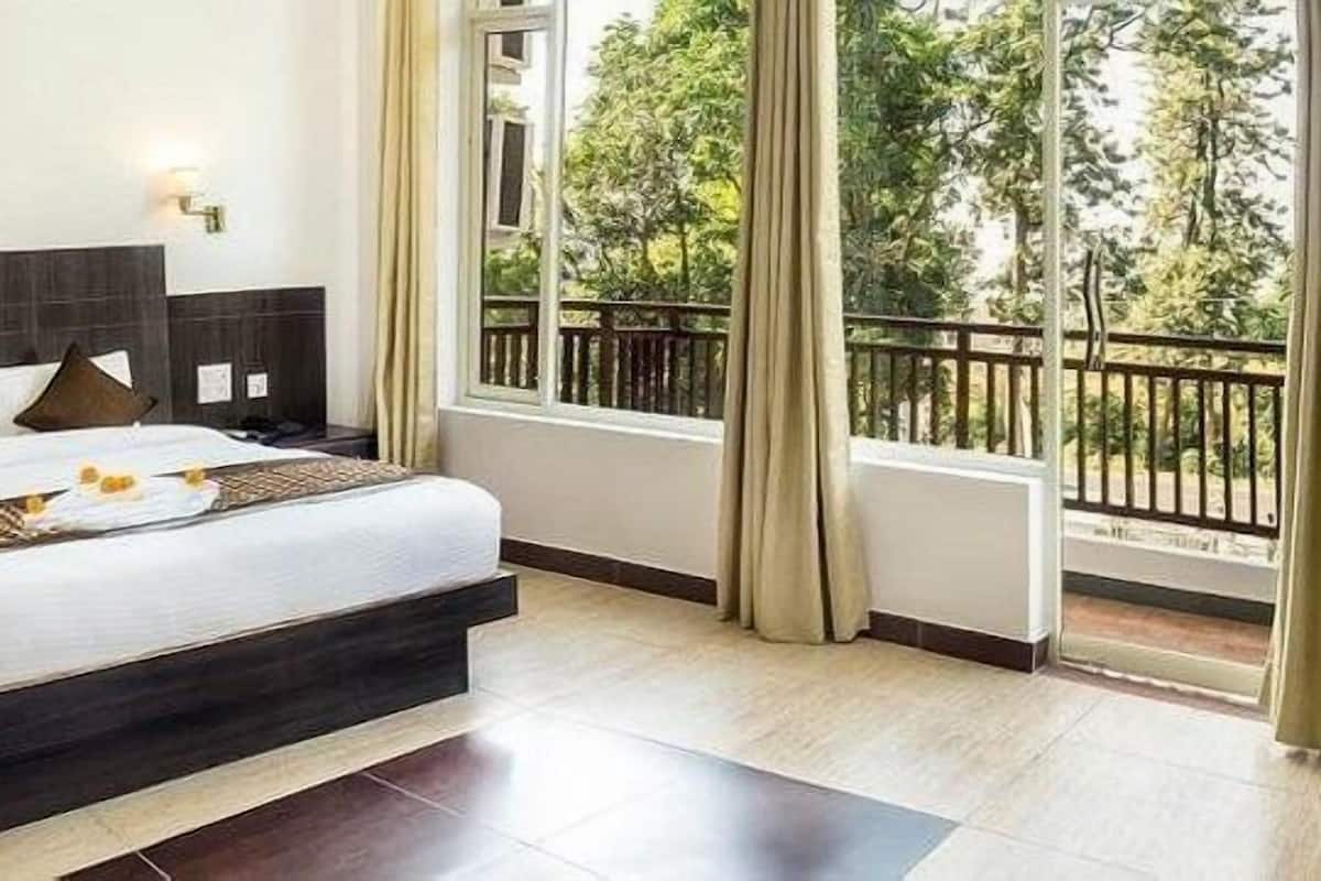 A hotel room with a large bed, a view of trees through a balcony, and a dark wood headboard.