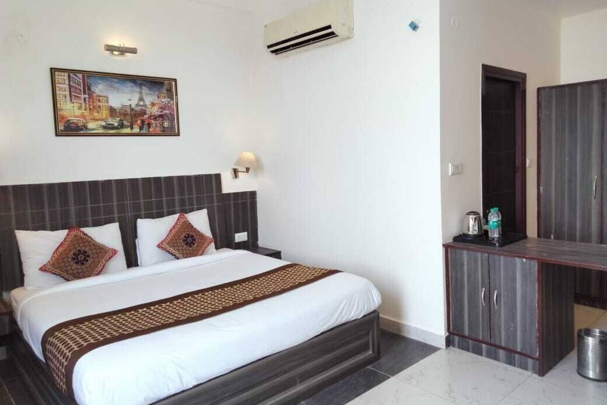 A hotel room with a bed, a painting on the wall, an air conditioner, and a small cabinet.