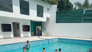 A swimming pool with a clear blue water, surrounded by a white building with a green door and windows. - Novel Resort by Urban (Ramnagar)