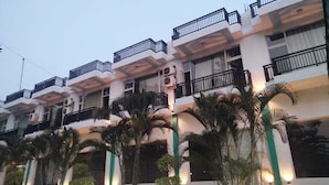 A multi-story hotel with balconies, air conditioning units, and a well-lit facade. - Novel Resort by Urban (Ramnagar)