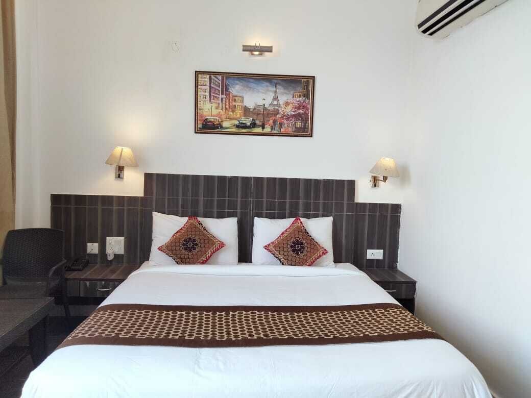 A hotel room with a large bed, two bedside lamps, a nightstand, a chair, and a painting on the wall.