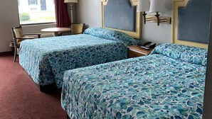 Ein Hotelzimmer mit zwei Betten, einem Schreibtisch, einem Stuhl und einem Fenster mit Blick auf ein Gebäude.