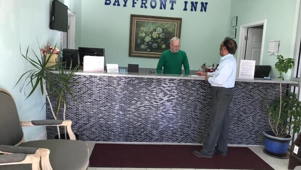 Ein Empfangstresen im Bayfront Inn mit einer Fliesenwand, einem floralen Bild in einem Rahmen und einem Fernseher darüber.