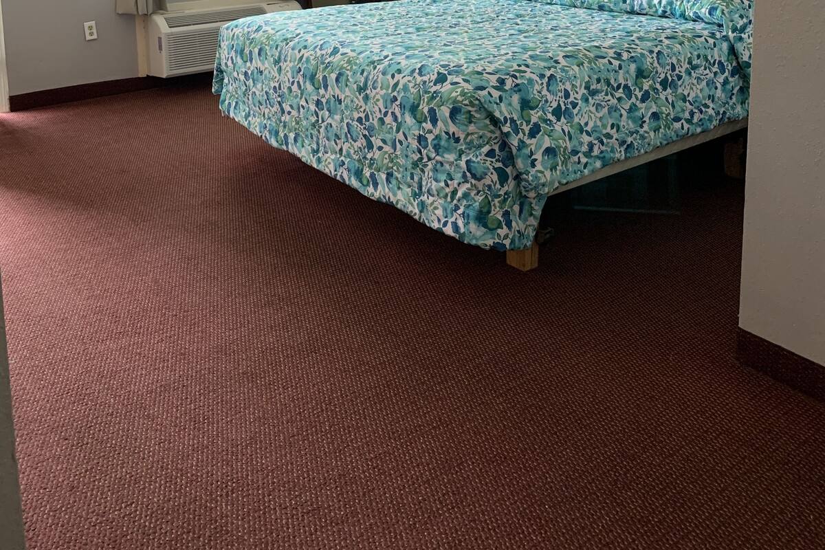 Quarto de hotel com uma cama, uma escrivaninha, uma cadeira, uma janela e um quadro na parede.