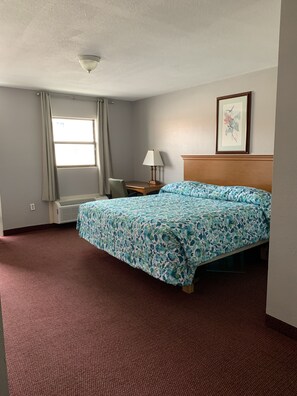 A hotel room with a bed, a desk, a chair, a window, and a framed picture on the wall.