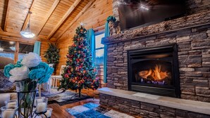 Un interior de cabaña acogedor con chimenea de piedra, un árbol de Navidad y techo de madera.