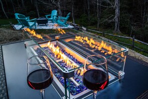 A glass-top outdoor grill with two glasses of red wine on it, surrounded by a wooden deck and chairs.