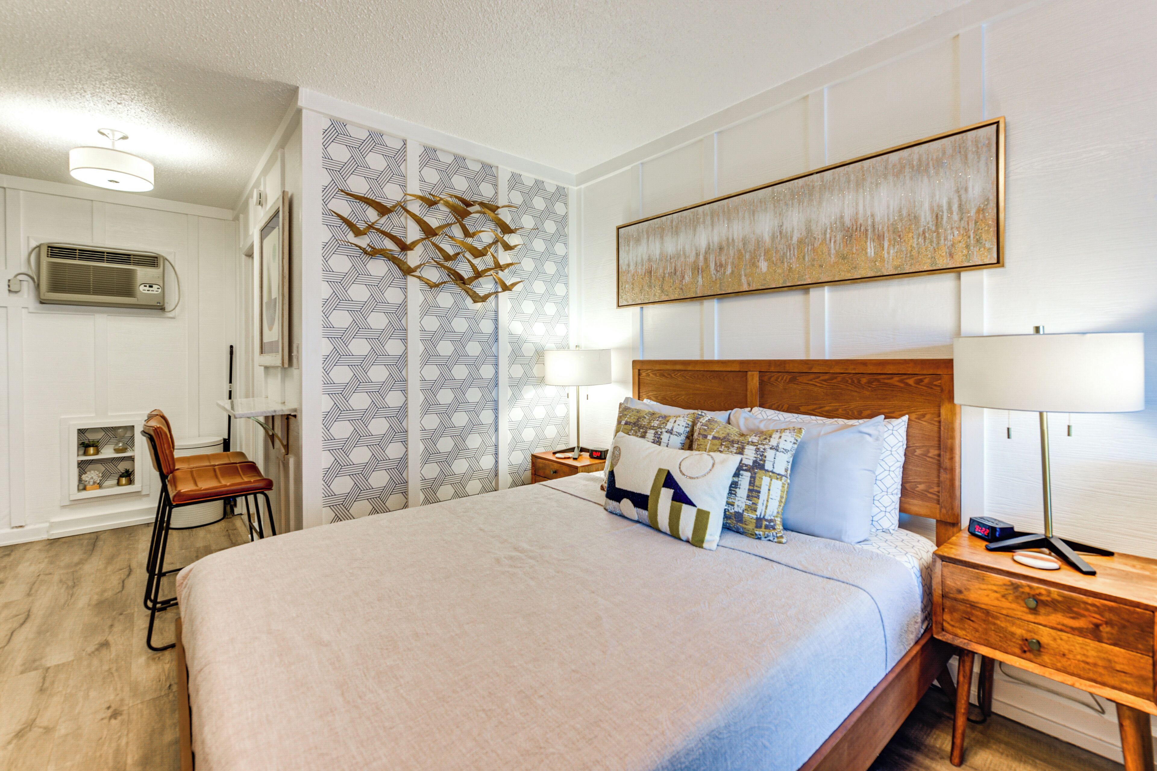 A neatly arranged bedroom with a large bed, bedside tables, a chair, and a wall-mounted air conditioning unit.