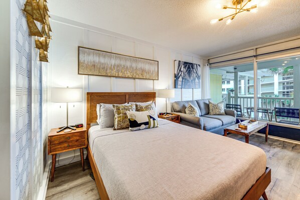 A hotel room with a large bed, a sofa, a desk, and a view of the outside.
