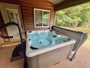A hot tub in a covered outdoor area with a wooden cabin structure, a window, and a door.