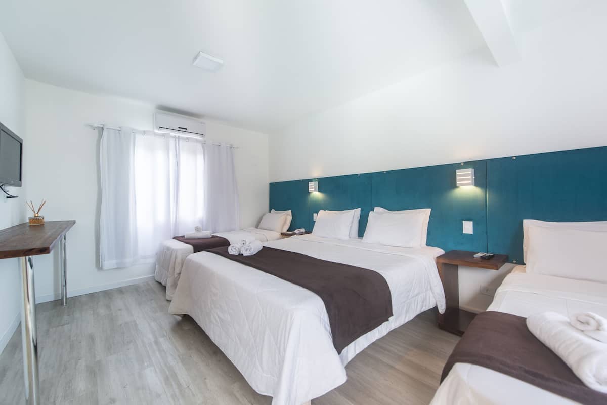A hotel room with two beds, a desk, a TV, and a window with curtains.