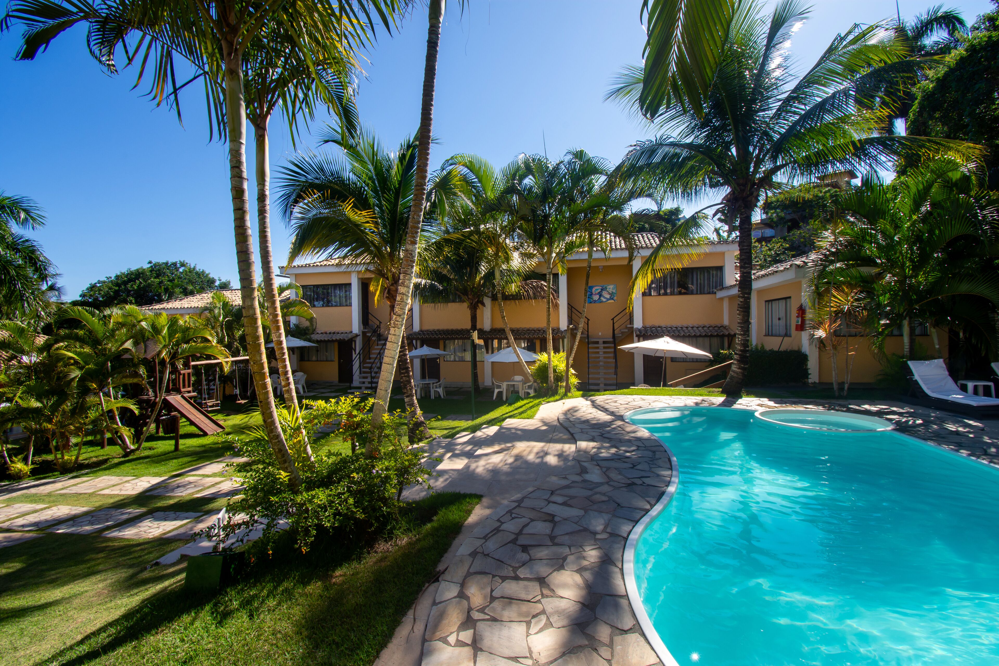 A pool area with a stone pathway, palm trees, and a building with multiple balconies.