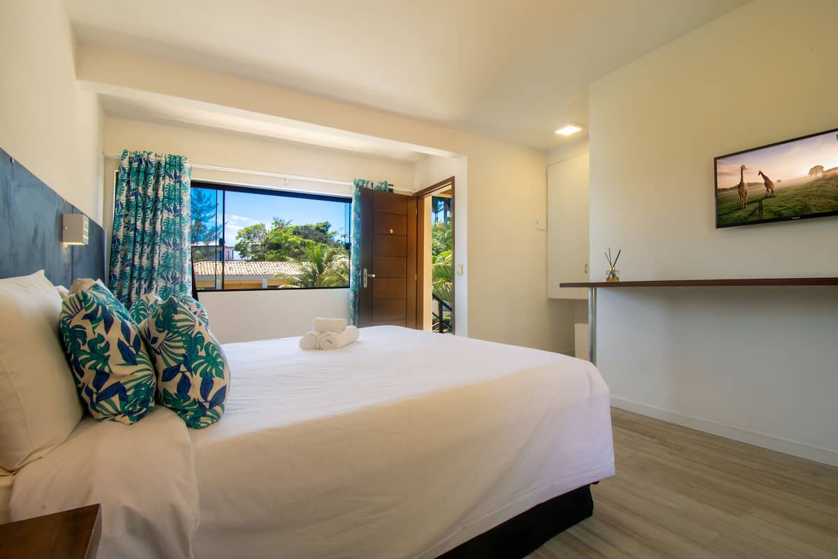 A hotel room with a large bed, a view of the outdoors, a painting on the wall, and a wooden floor.