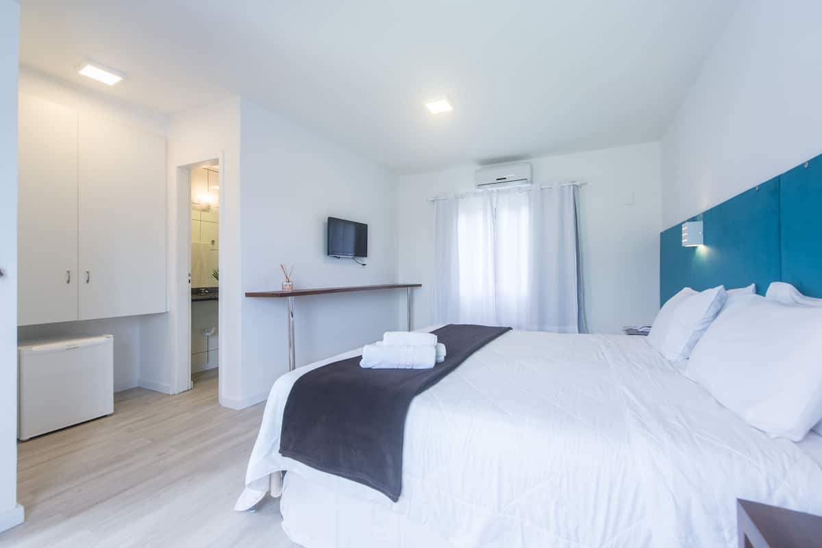 A bedroom with a bed, a desk, a television, and an air conditioning unit.