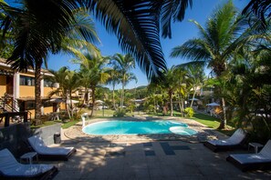 Uma área de piscina com espreguiçadeiras, palmeiras e um céu azul límpido.
