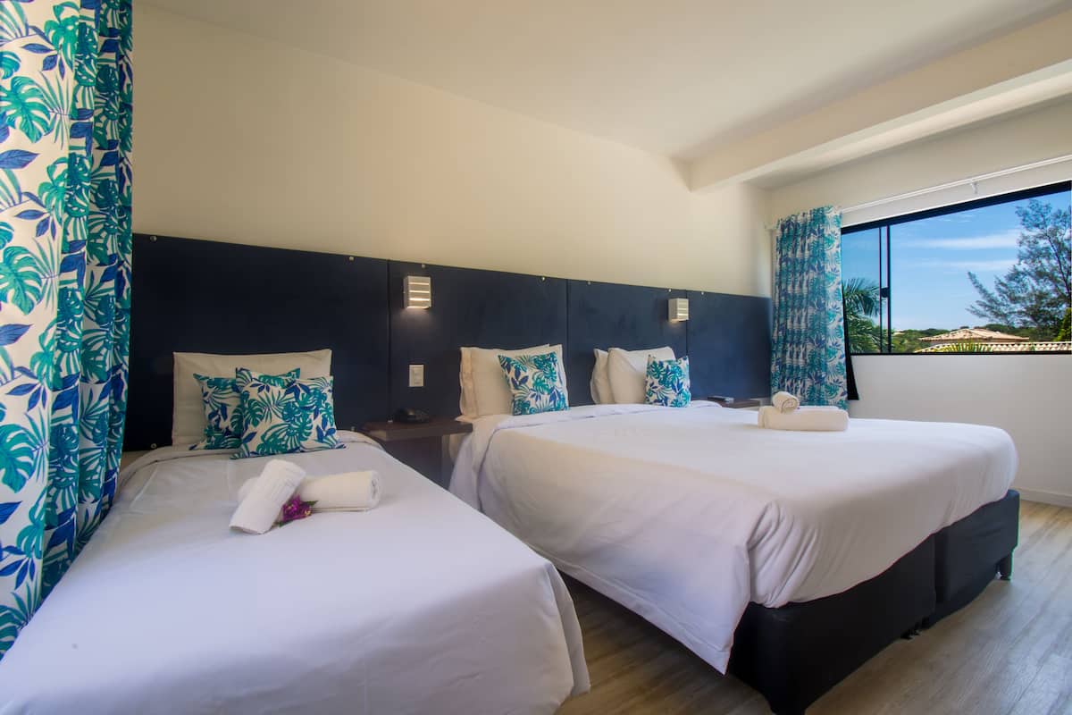 A hotel room with two beds, a dark headboard, and a large window with a view of the outdoors.