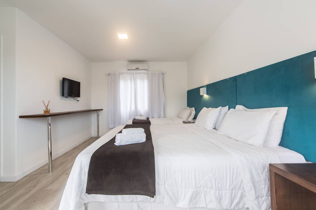 A hotel room with a bed, a desk, a TV, and an air conditioning unit.
