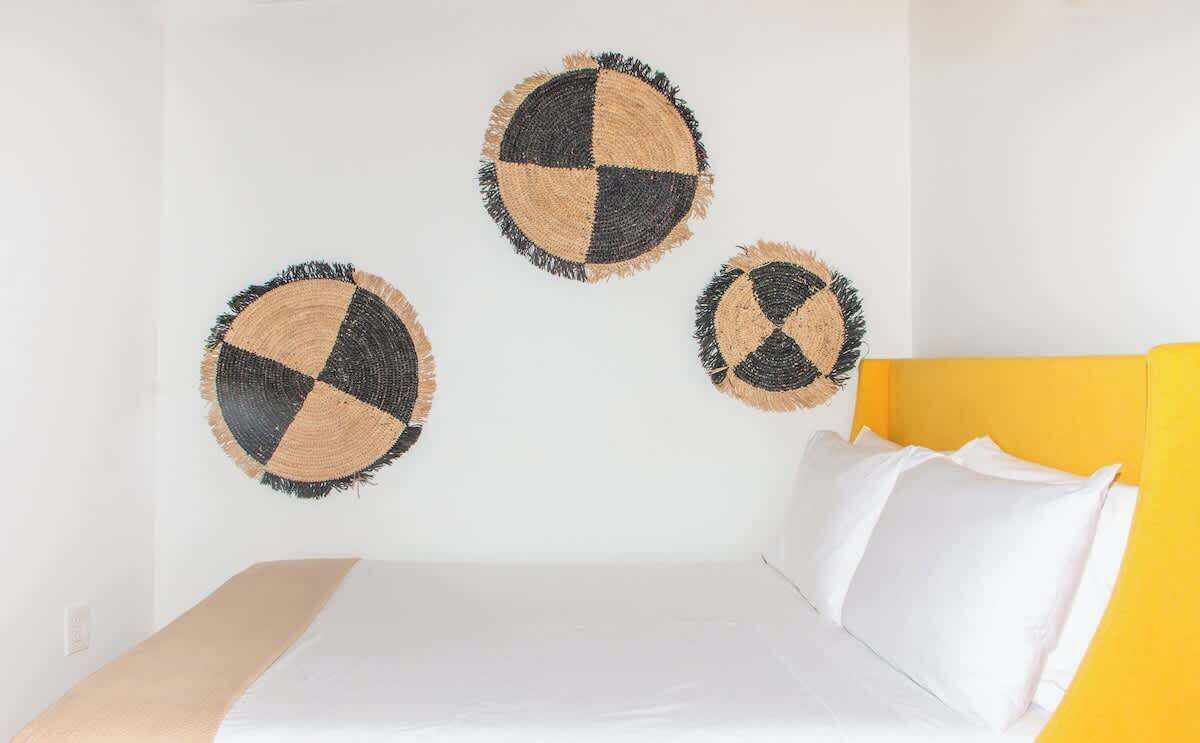 A bed with white bedding and a yellow headboard, accompanied by three wall-mounted circular wall art pieces.