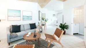Een moderne woonkamer met een bank, salontafel en stoel, een eethoek met tafel en stoelen, en een keuken op de achtergrond.