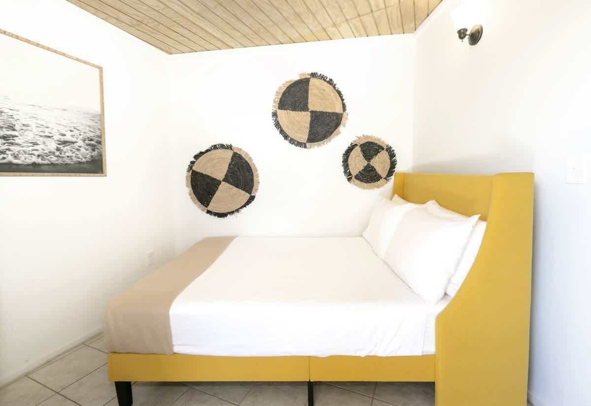Un lit avec une tête de lit jaune, une literie blanche et trois éléments de décoration circulaire fixés au mur.