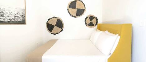 Un lit avec une tête de lit jaune, une literie blanche et trois éléments de décoration circulaire fixés au mur.