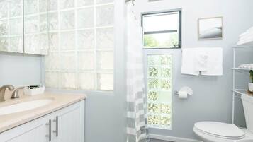 Un bagno con lavandino bianco, specchio e water. Si vede del verde attraverso una finestra.