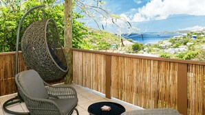 Een balkon met rieten meubilair, een hangstoel en uitzicht op de oceaan en verre gebouwen.