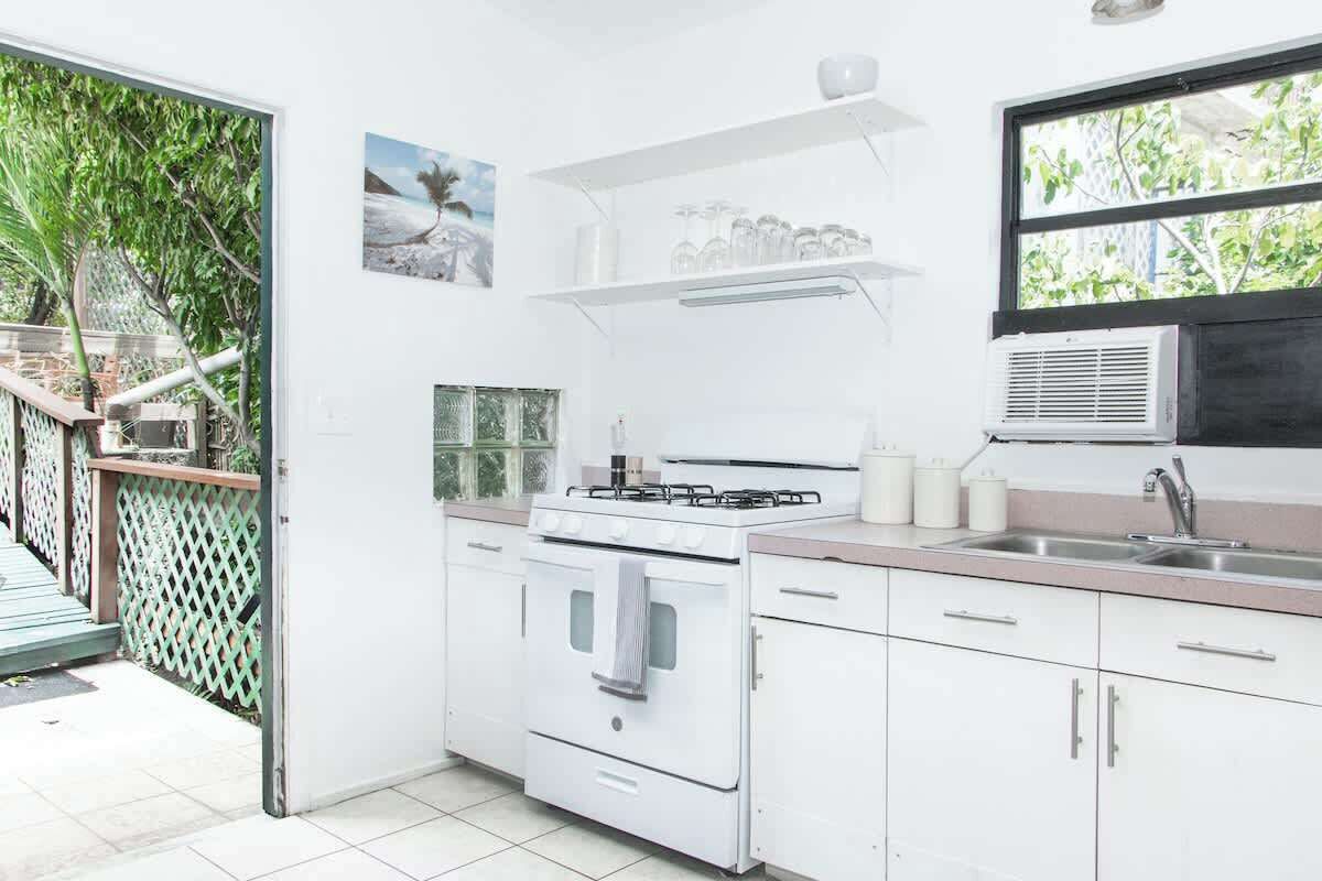 A modern kitchen with white cabinets, a gas stove, and a sink. There is a window with a view of greenery outside.