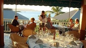 Une table dressée pour un repas, avec vue sur l’océan, entourée de chaises en osier.